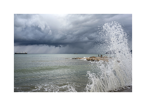 Eine Welle vor ein paar Spaziergaengern am Strand von Bar in Montenegro